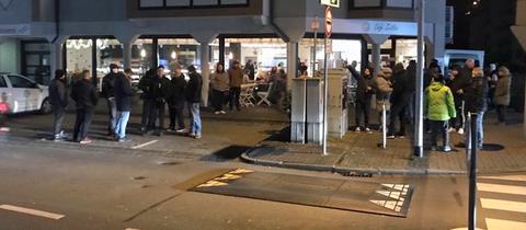 Menschen stehen in Grüppchen vor einer Bäckerei.