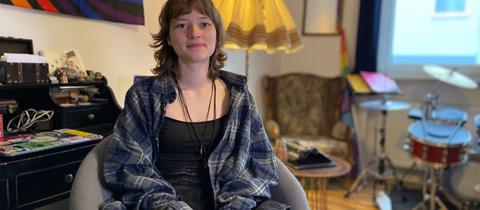 Claire Duda, eine junge Frau, sitzt auf einem Sessel in einem Zimmer und lächelt verhalten