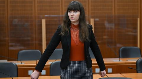 Eine junge Frau mit dunklen Haaren steht in einem Gerichtssaal.