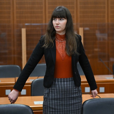 Eine junge Frau mit dunklen Haaren steht in einem Gerichtssaal.