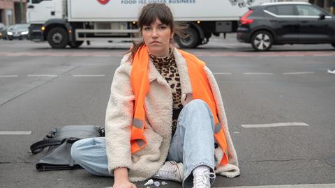 Eine junge Frau mit einer Warnweste hat sich auf einer Straße festgeklebt.