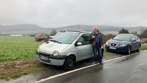 Mann lehnt an grauen Twingo am Feldrand