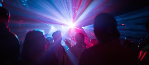 Silhoutten von tanzenden Menschen im bunten Licht einer Discothek.