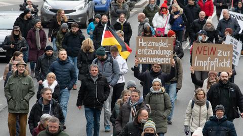 Menschen laufen auf einer Straße, einer hält ein Schild mit der Aufschrift "Nein zur Impfpflicht" hoch