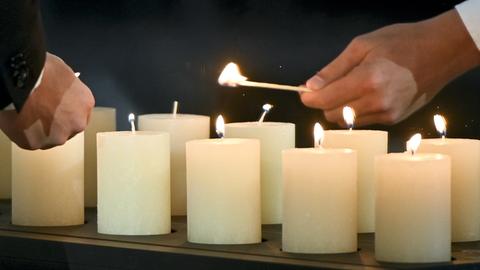 Viele brenndene weiße Kerzen. Zwei Hände in Großaufnahme mit Streichhölzern, welche die Kerzen anzünden.