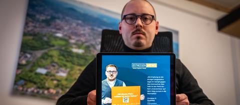 Chefredakteur Christian Stadtfeld sitzt am Schreibtisch und zeigtauf einem Laptop, wie Webseite, auf welcher er mit einem Hitlerschnurrbart dargestellt wird.