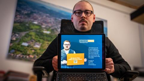 Chefredakteur Christian Stadtfeld sitzt am Schreibtisch und zeigtauf einem Laptop, wie Webseite, auf welcher er mit einem Hitlerschnurrbart dargestellt wird.