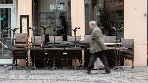 Ein älterer Mann mit Glatze und Brille eilt an einem geschlossenen Lokal in Wiesbaden vorbei. Vor der Gaststätte sind Tische und Stühle zusammengeräumt und angekettet.