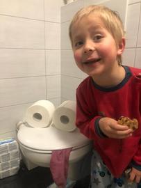 Der kleine Junge Nils vor einer Toilettenschüssel, die er mithilfe von Klopapierrollen und einem Tuch als Gesicht gestaltet hat
