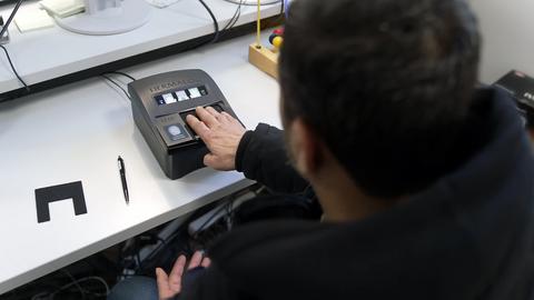 Ein dunkelhaariger Mann (von hinten zu sehen) legt seine Hand auf einen Fingerabdruck-Scanner in der Erstaufnahmeeinrichtung in Gießen