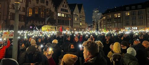 Menschen halten bei der Demo gegen rechts auf dem Frankfurter Römerberg abends Lichter in die Höhe.