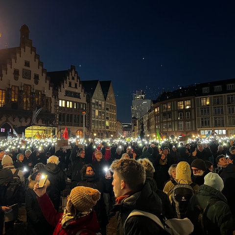 Menschen halten bei der Demo gegen rechts auf dem Frankfurter Römerberg abends Lichter in die Höhe.