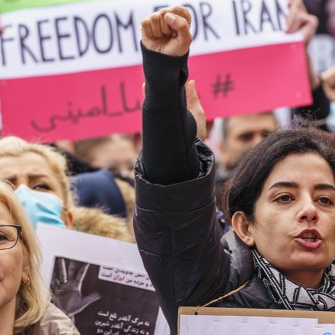 Menschen recken ihre Fäuste vor einem Plakat mit der Aufschrift "Freedom for Iran".