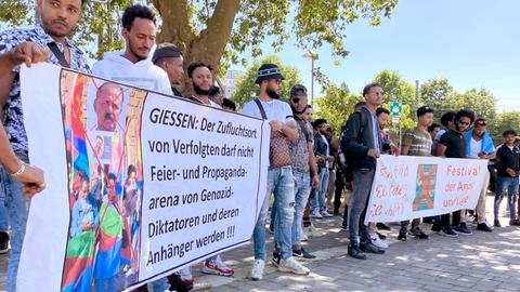 Menschen stehen nebeneinander in Reihe und halten zwei Banner hoch. Auf einem steht: "Gießen: Der Zufluchtsort von Verfolgten darf nicht Feier- und Propagandaarena von Genozid-Diktatoren und deren Anhänger werden".