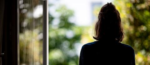 Frau steht am offenen Fenster und schaut raus. Wie sehen sie von hinten.