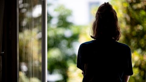 Frau steht am offenen Fenster und schaut raus. Wie sehen sie von hinten.