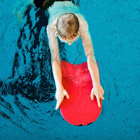 Ein Junge schwimmt mit einem Schwimmbrett in einem Schwimmbecken.
