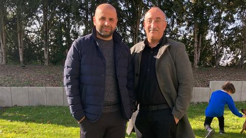 Nedim Tosun und Zeki Yildirim - zwei Männer auf einer grünen Wiese. Im Hintergrund spielt ein Kind mit einem Hund. 