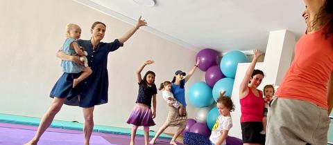 Tanzende Mütter und Kinder auf Schaumstoffmatten in einem Gymnastikraum.