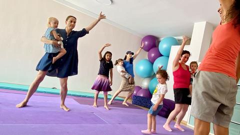 Tanzende Mütter und Kinder auf Schaumstoffmatten in einem Gymnastikraum.