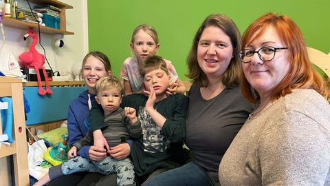 Zwei Frauen und vier Kinder haben sich in einem Kinderzimmer zusammengesetellt und lachen in die Kamera.
