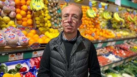 Ein Mann mit Brille steht vor einem Gemüseregal.