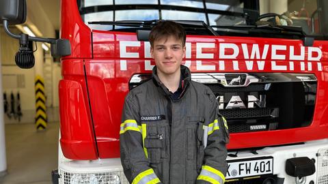 Frederic Charrier - junger Feuerwehrmann, kurzes dunkler Haar, lehnt an der Front eines Feuerwehrautos. In den Händen hält er einen Feuerwehrhelm. 