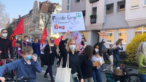 In einem Demonstrationszug hält eine junge Frau ein Schild hoch mit der Aufschrift "Fossile Energie finanziert Krieg".
