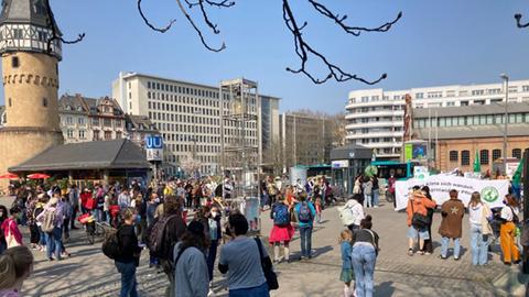 Eine Menschenmenge steht an der Bockenheimer Warte, links ist der Turm der Warte zu sehen. 