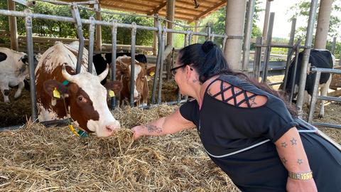 Bewohnerin vom Hof Fleckenbühl füttert eine Kuh, die im Außenstall steht, mit Stroh