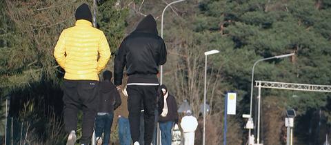 Eine Gruppe männlicher Asylbewerber in Jogginghosen und Jacken läuft eine Straße entlang, man sieht sie nur von hinten. 