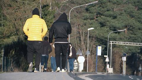 Eine Gruppe männlicher Asylbewerber in Jogginghosen und Jacken läuft eine Straße entlang, man sieht sie nur von hinten. 