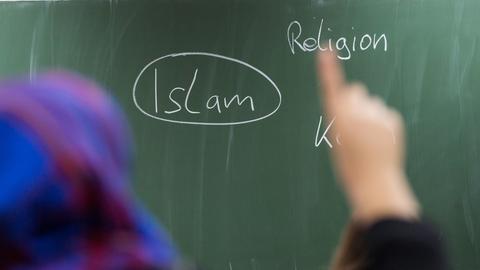 Eine Schülerin mit Kopftuch meldet sich im Unterricht. An der Tafel prangt das Wort "Islam"