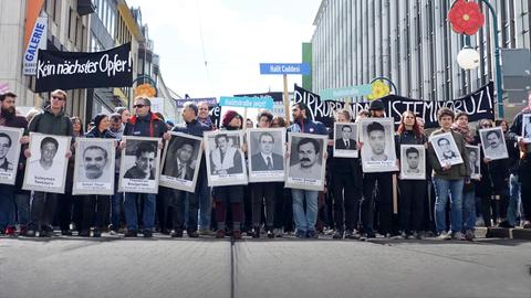 Demonstrierende gehen in Reihe in einer Fußgängerzone und tragen Portraits der Ermordeten vor ihren Körpern.