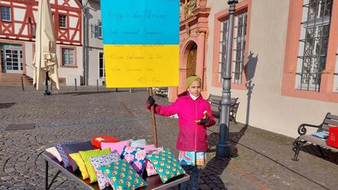Mädchen mit Ukraine-Flagge und selbstgenähten Kissen auf einem Tisch vor ihr.