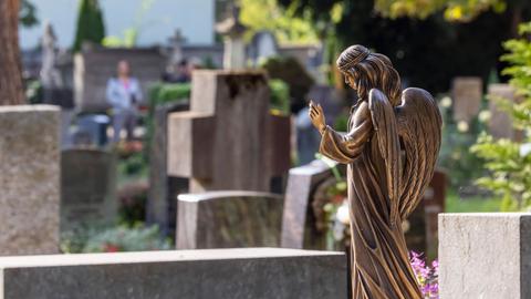 Engelsfigur vor mehreren Grabsteinen auf Friedhof