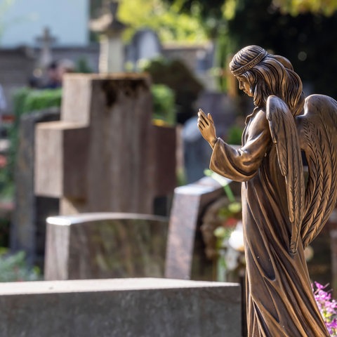 Engelsfigur vor mehreren Grabsteinen auf Friedhof