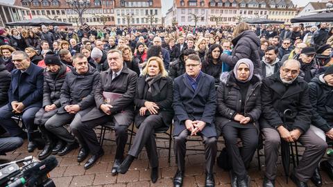 Claus Kaminsky (SPD, 4.v.l), Oberbürgermeister von Hanau, Nancy Faeser (SPD, 5.v.l), Bundesinnenministerin, und Boris Rhein (CDU, M), Ministerpräsident von Hessen, sitzen neben Angehörigen der Opfer bei einer Gedenkstunde auf dem Marktplatz