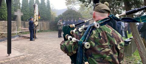 Ein Dudelsackspieler in Uniform steht vor dem Gedenken zum Volkstrauertag