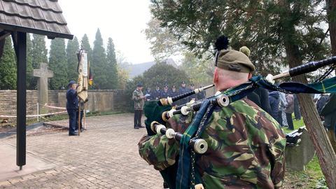 Ein Dudelsackspieler in Uniform steht vor dem Gedenken zum Volkstrauertag