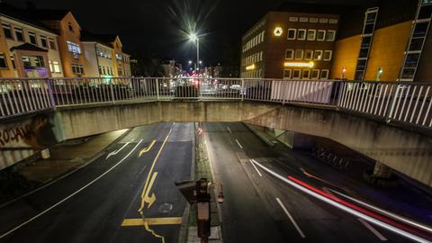 Eine Straßenkreuzung im dunklen, darüber eine Fußgängerbrücke. Rechts und links Ampeln