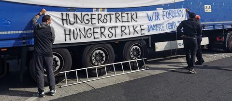 Zwei Männer hängen ein Banner mit der Aufschrift "Hungerstreik" an einem Lkw auf.