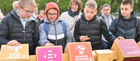 Schüler aus Hofbieber drehen Würfel mit Fragen und Antworten im Grünen Klassenzimmer bei der Landesgartenschau, im Hintergrund Umweltministerin Priska Hinz