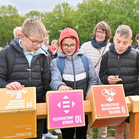 Schüler aus Hofbieber drehen Würfel mit Fragen und Antworten im Grünen Klassenzimmer bei der Landesgartenschau, im Hintergrund Umweltministerin Priska Hinz