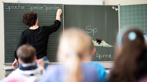 Eine Lehrerin schreibt in einer Grundschule Wörter mit "Sp" am Anfang an eine Tafel.