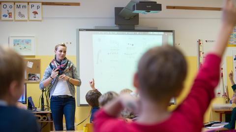 Grundschullehrerin vor einem Whiteboard, im Vordergrund Grundschüler