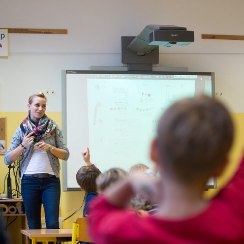 Grundschullehrerin vor einem Whiteboard, im Vordergrund Grundschüler
