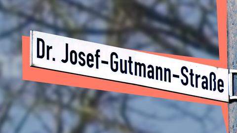 Straßenschild mit der Beschriftung "Dr. Josef-Gutmann-Straße". Hinter dem Straßenschild liegt eine farbige Fläche, dahinter unscharf leicht verfärbt Strukturen eines Baumes.