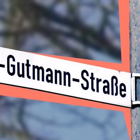 Straßenschild mit der Beschriftung "Dr. Josef-Gutmann-Straße". Hinter dem Straßenschild liegt eine farbige Fläche, dahinter unscharf leicht verfärbt Strukturen eines Baumes.