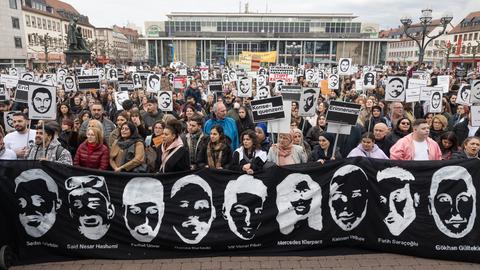 Menschen halten Bilder und Banner mit Gesichtern der Opfer von Hanau hoch
